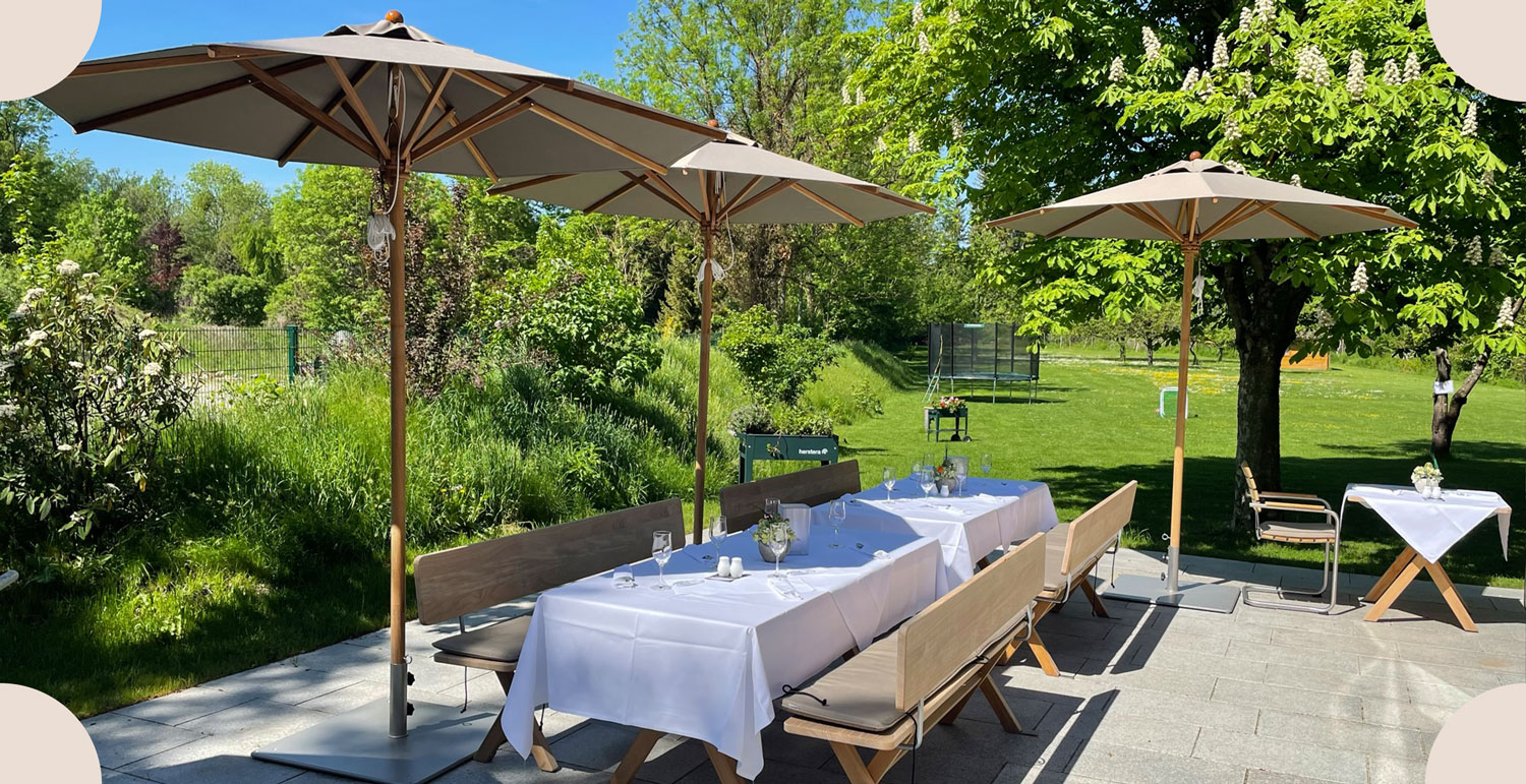 Holzbänke und weiß eingedeckter Tisch im Sommer mit Blick in den Garten