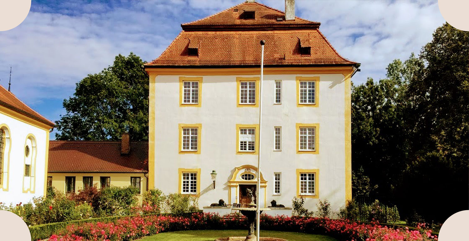 Weißes Schloss mit gelben Fensterrahmen und Park mit Rosen